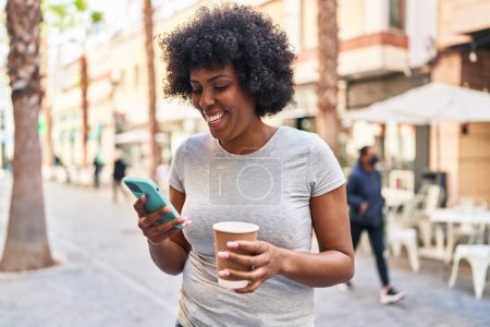 Téléchargez les photos : Femme afro-américaine utilisant smartphone boire du café dans la rue - en image libre de droit
