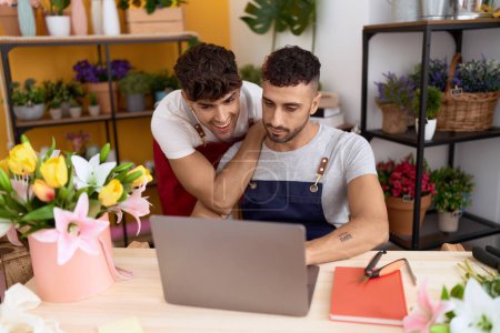 Téléchargez les photos : Two hispanic men florists smiling confident using laptop working at flower shop - en image libre de droit