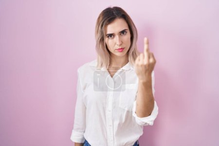 Foto de Young beautiful woman standing over pink background showing middle finger, impolite and rude fuck off expression - Imagen libre de derechos