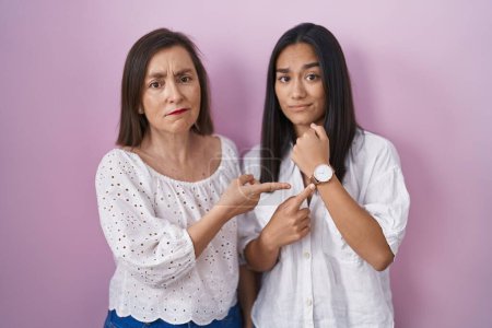 Foto de Hispanic mother and daughter together in hurry pointing to watch time, impatience, looking at the camera with relaxed expression - Imagen libre de derechos