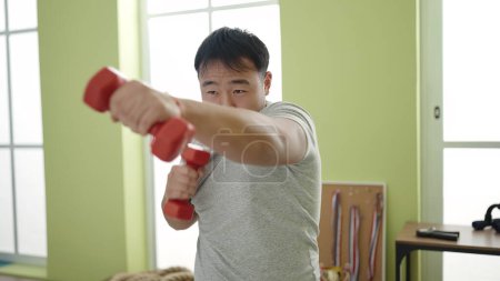 Téléchargez les photos : Jeune homme chinois utilisant des haltères boxe au centre sportif - en image libre de droit