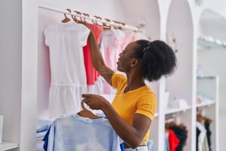 Foto de Mujer afroamericana asistente de tienda colgando ropa en estante en la tienda de ropa - Imagen libre de derechos