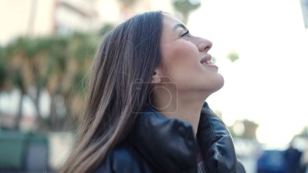 Téléchargez les photos : Jeune belle femme hispanique souriant confiant regardant le ciel dans la rue - en image libre de droit