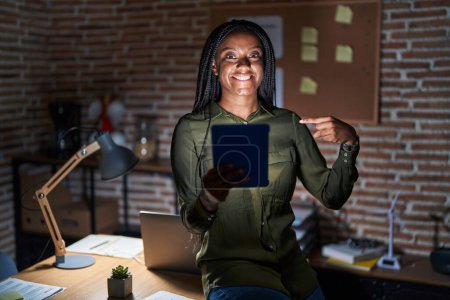 Photo for Young african american with braids working at the office at night looking confident with smile on face, pointing oneself with fingers proud and happy. - Royalty Free Image