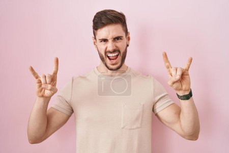 Téléchargez les photos : Hispanic man with beard standing over pink background shouting with crazy expression doing rock symbol with hands up. music star. heavy music concept. - en image libre de droit