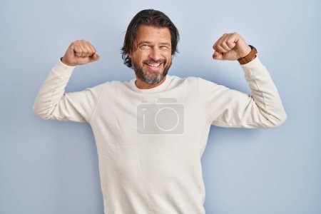 Photo for Handsome middle age man wearing casual sweater over blue background showing arms muscles smiling proud. fitness concept. - Royalty Free Image
