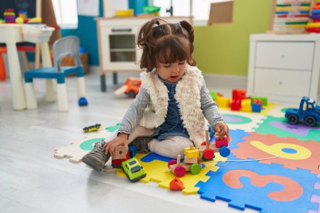 Foto de Adorable niño hispano jugando con el juguete del coche sentado en el suelo en el jardín de infantes - Imagen libre de derechos