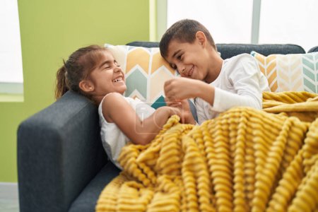 Foto de Hermano y hermana riendo por cosquillas sentados en el sofá en casa - Imagen libre de derechos