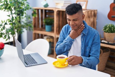 Téléchargez les photos : Young latin man using laptop suffering for throat pain at home - en image libre de droit