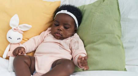 Téléchargez les photos : African american baby sitting on bed with relaxed expression at bedroom - en image libre de droit