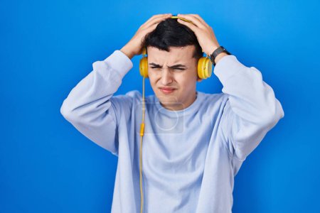 Téléchargez les photos : Personne non binaire écoutant de la musique à l'aide d'écouteurs souffrant de maux de tête désespérés et stressés parce que la douleur et la migraine. mains sur la tête. - en image libre de droit