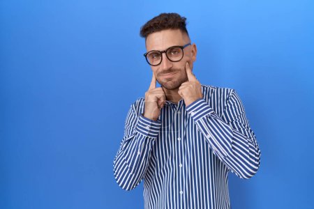 Photo for Hispanic man with beard wearing glasses smiling with open mouth, fingers pointing and forcing cheerful smile - Royalty Free Image