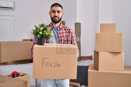 Téléchargez les photos : Middle east man with beard moving to a new home holding cardboard box relaxed with serious expression on face. simple and natural looking at the camera. - en image libre de droit