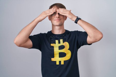 Photo for Caucasian blond man wearing bitcoin t shirt covering eyes with hands smiling cheerful and funny. blind concept. - Royalty Free Image