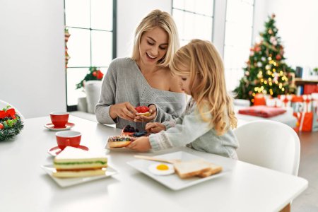 Photo for Mother and daughter having breakfast sitting by christmas tree at home - Royalty Free Image