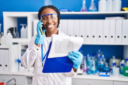 Foto de Mujer afroamericana vistiendo uniforme científico hablando en el laboratorio de teléfonos inteligentes - Imagen libre de derechos