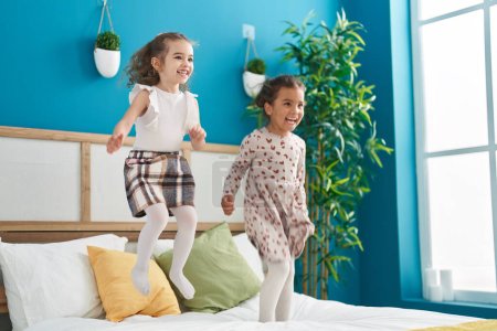Téléchargez les photos : Deux enfants souriants confiants sautant sur le lit dans la chambre - en image libre de droit