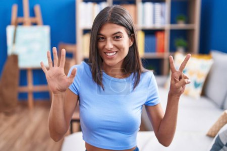 Foto de Brunette young woman sitting on the sofa at home showing and pointing up with fingers number seven while smiling confident and happy. - Imagen libre de derechos