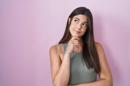 Photo for Hispanic woman standing over pink background with hand on chin thinking about question, pensive expression. smiling with thoughtful face. doubt concept. - Royalty Free Image
