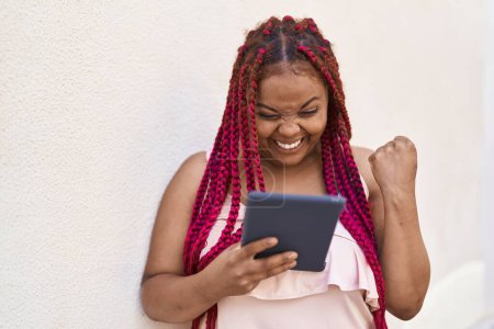 Téléchargez les photos : Afro-américaine femme souriant confiant en utilisant touchpad à la rue - en image libre de droit