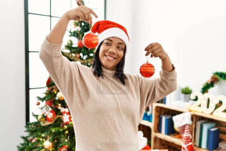 Photo for Hispanic brunette woman holding christmas decorations at home - Royalty Free Image
