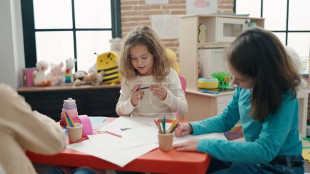 Foto de Two kids students sitting on table drawing on paper at kindergarten - Imagen libre de derechos