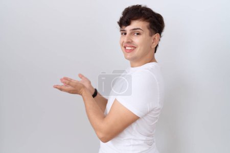 Téléchargez les photos : Young non binary man wearing casual white t shirt pointing aside with hands open palms showing copy space, presenting advertisement smiling excited happy - en image libre de droit