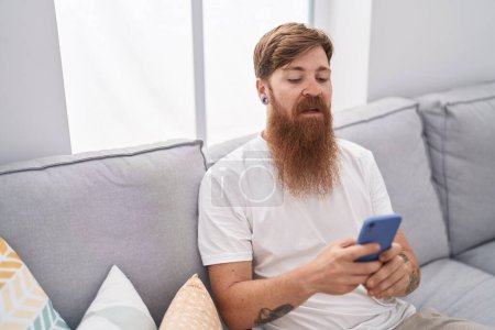Photo for Young redhead man using smartphone with serious expression at home - Royalty Free Image