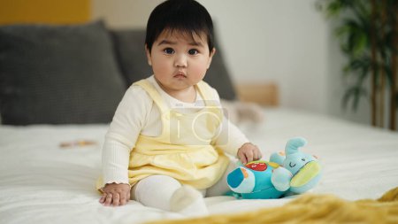 Téléchargez les photos : Adorable hispanic baby playing with elephant doll sitting on bed at bedroom - en image libre de droit
