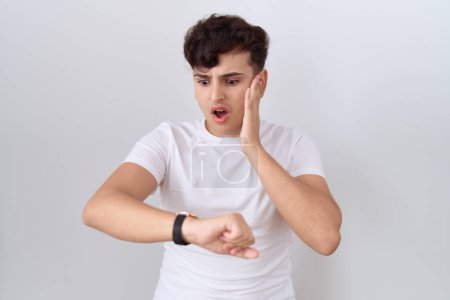 Foto de Joven hombre no binario con camiseta blanca casual mirando el tiempo reloj preocupado, miedo de llegar tarde - Imagen libre de derechos