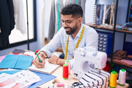 Téléchargez les photos : Young arab man tailor smiling confident drawing on notebook at tailor shop - en image libre de droit