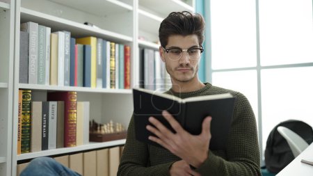 Téléchargez les photos : Jeune homme hispanique étudiant lecture livre étudiant à la bibliothèque université - en image libre de droit