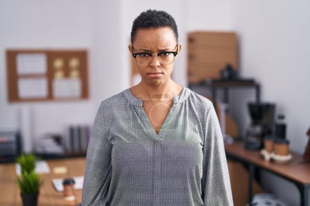Foto de African american woman working at the office wearing glasses skeptic and nervous, frowning upset because of problem. negative person. - Imagen libre de derechos