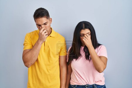 Foto de Young couple standing over isolated background tired rubbing nose and eyes feeling fatigue and headache. stress and frustration concept. - Imagen libre de derechos