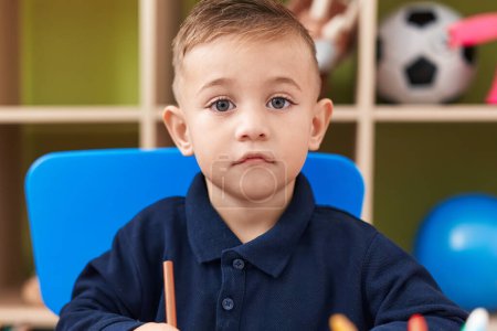 Foto de Adorable niño hispano estudiante de preescolar sentado en el dibujo de la mesa en papel en el jardín de infantes - Imagen libre de derechos