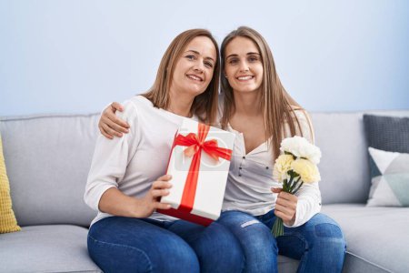 Foto de Dos mujeres madre e hija sorprenden con regalo de cumpleaños y flores en casa - Imagen libre de derechos