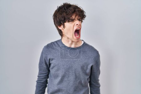 Photo for Young man standing over isolated background angry and mad screaming frustrated and furious, shouting with anger. rage and aggressive concept. - Royalty Free Image