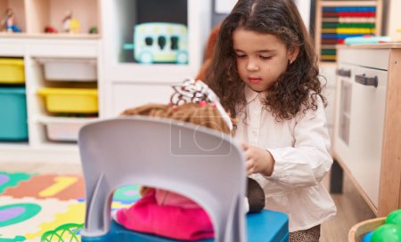 Photo for Adorable hispanic girl playing with doll at kindergarten - Royalty Free Image