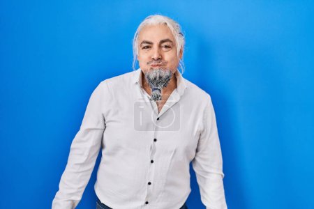Photo for Middle age man with grey hair standing over blue background puffing cheeks with funny face. mouth inflated with air, crazy expression. - Royalty Free Image