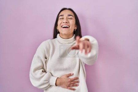 Téléchargez les photos : Young south asian woman standing over pink background laughing at you, pointing finger to the camera with hand over body, shame expression - en image libre de droit