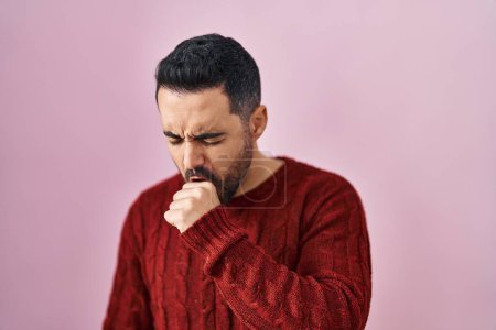 Foto de Hombre hispano joven con barba usando suéter casual sobre fondo rosa sintiéndose mal y tosiendo como síntoma de resfriado o bronquitis. concepto de atención sanitaria. - Imagen libre de derechos