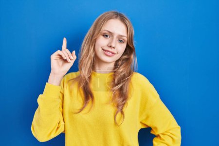 Téléchargez les photos : Jeune femme caucasienne debout sur fond bleu pointant du doigt avec une idée réussie. Sorti et heureux. numéro un. - en image libre de droit