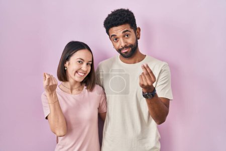 Téléchargez les photos : Jeune couple hispanique ensemble sur fond rose faisant geste d'argent avec les mains, demandant le paiement du salaire, entreprise millionnaire - en image libre de droit