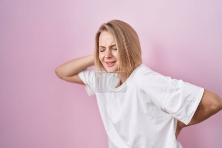 Photo for Young caucasian woman standing over pink background suffering of backache, touching back with hand, muscular pain - Royalty Free Image