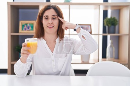 Photo for Brunette woman drinking glass of orange juice smiling pointing to head with one finger, great idea or thought, good memory - Royalty Free Image