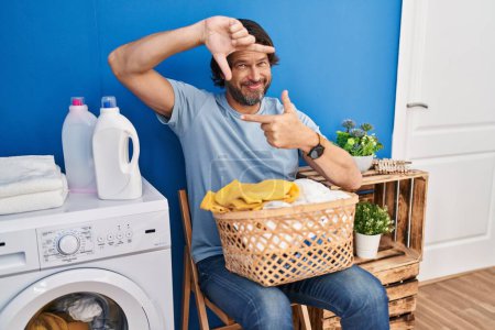 Foto de Handsome middle age man waiting for laundry smiling making frame with hands and fingers with happy face. creativity and photography concept. - Imagen libre de derechos