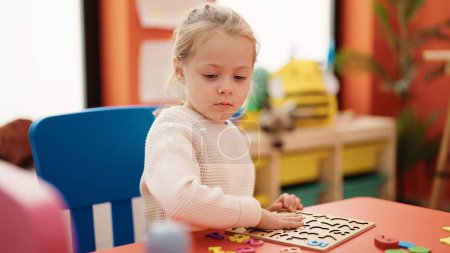 Téléchargez les photos : Adorable fille blonde jouer avec des mathématiques jeu de puzzle assis sur la table à la maternelle - en image libre de droit