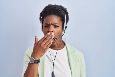 Foto de Mujer afroamericana con auriculares de agente de call center aburrida bostezando cansada cubriendo la boca con la mano. inquietud y somnolencia. - Imagen libre de derechos