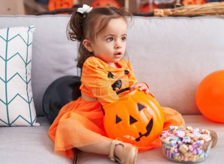 Téléchargez les photos : Adorable bambin hispanique ayant fête d'Halloween tenant des bonbons à la maison - en image libre de droit