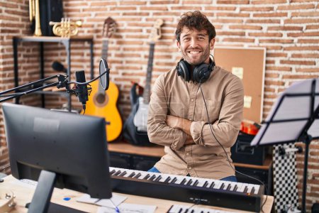 Foto de Young man musician smiling confident sitting with arms crossed gesture at music studio - Imagen libre de derechos